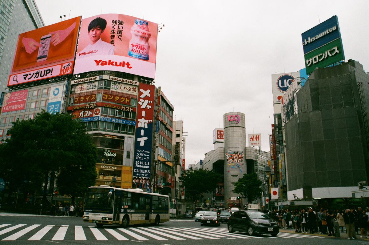 Pedestrians crossing Shibuya Scramble Crossing beneath large video billboards in Tokyo