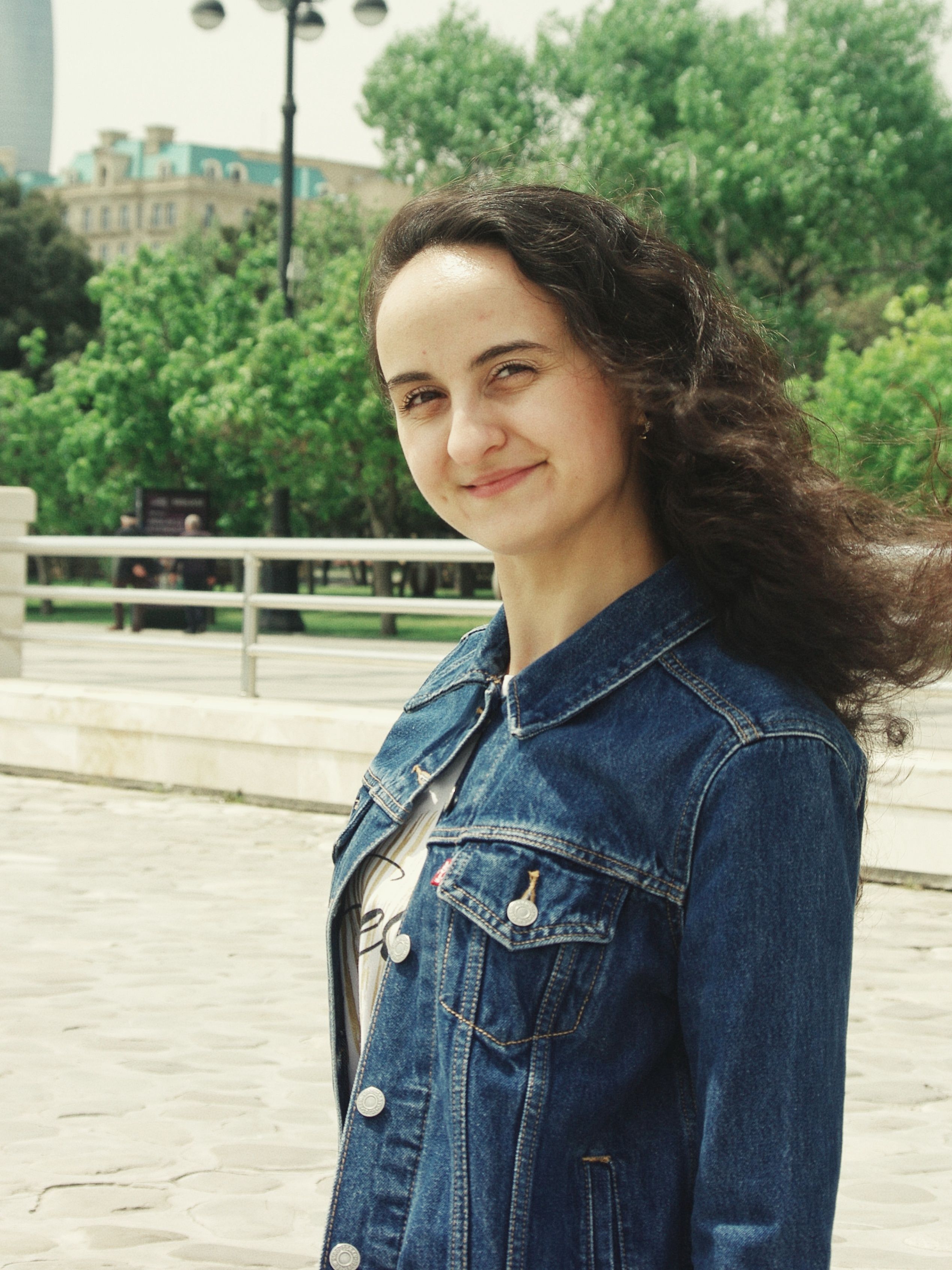 Portrait of a smiling woman in a denim jacket in a park in Baku, Azerbaijan.