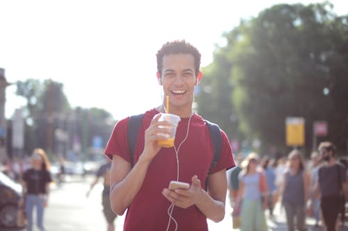 Free Man Wearing Red Shirt While Holding Plastic Cup and Smartphone Stock Photo