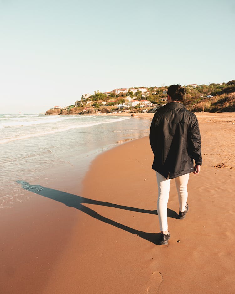 Man In Black Jacket And White Pants Walking On Beach