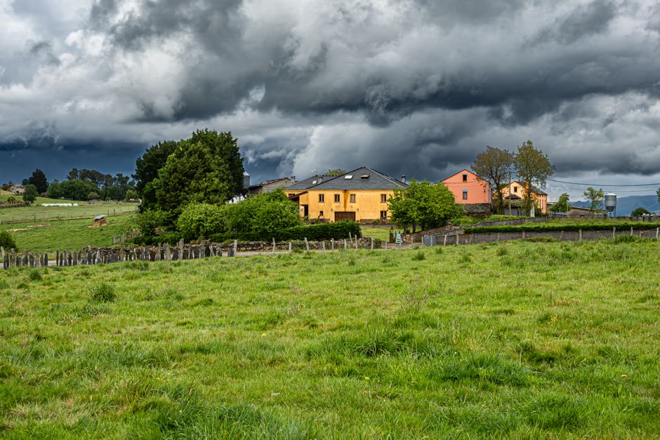 Escena rural dramática con casas coloridas y cielos tormentosos en un paisaje verde exuberante.