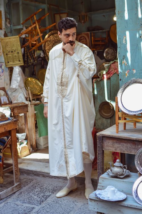 Free Man in white traditional gown stands in a Tunisian medina shop with decorative items. Stock Photo