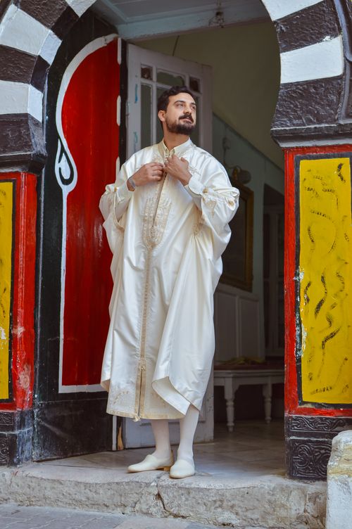 Free Man in traditional Tunisian clothing standing at colorful entrance of Medina. Stock Photo