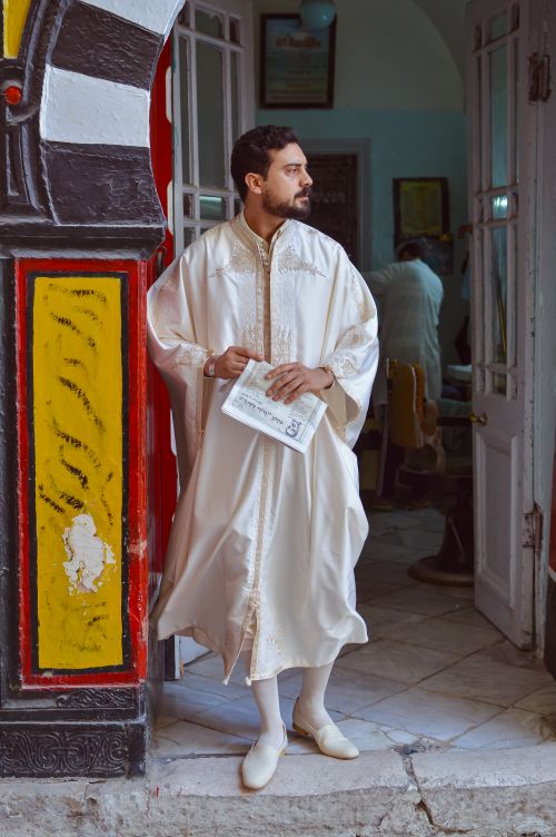 Free Man in traditional attire standing with a document in a doorway. Stock Photo