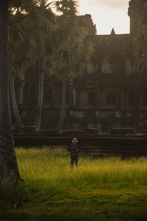 Free A person stands alone amid tall grass with Angkor Wat's ruins at sunrise in Cambodia. Stock Photo