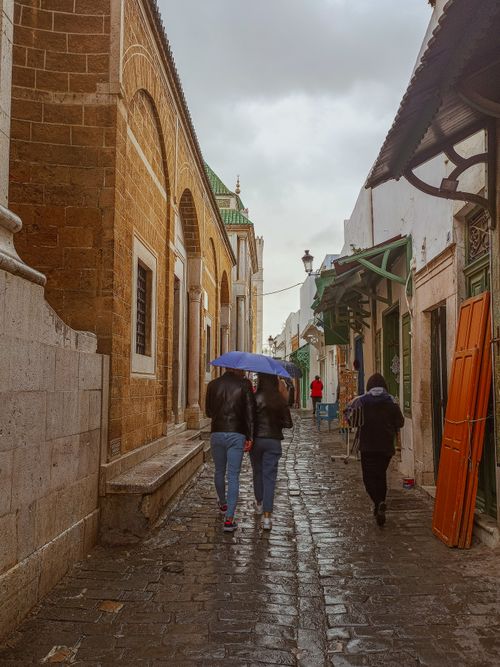 Free People walking with umbrellas in the historic Medina of Tunis, Tunisia, showcasing traditional architecture. Stock Photo
