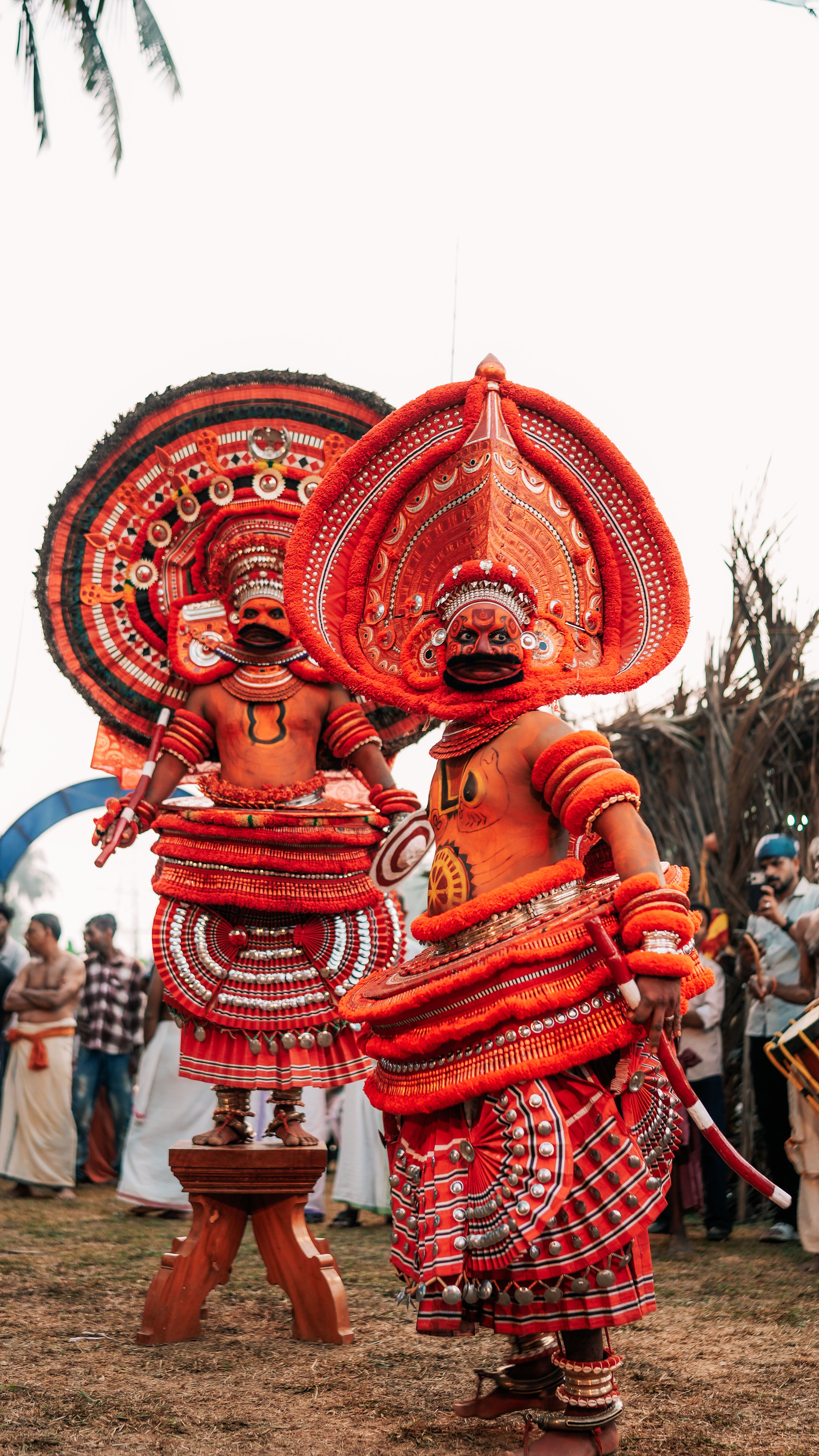 Colorful theyyam dancers in traditional costumes performing at an outdoor festival in India.