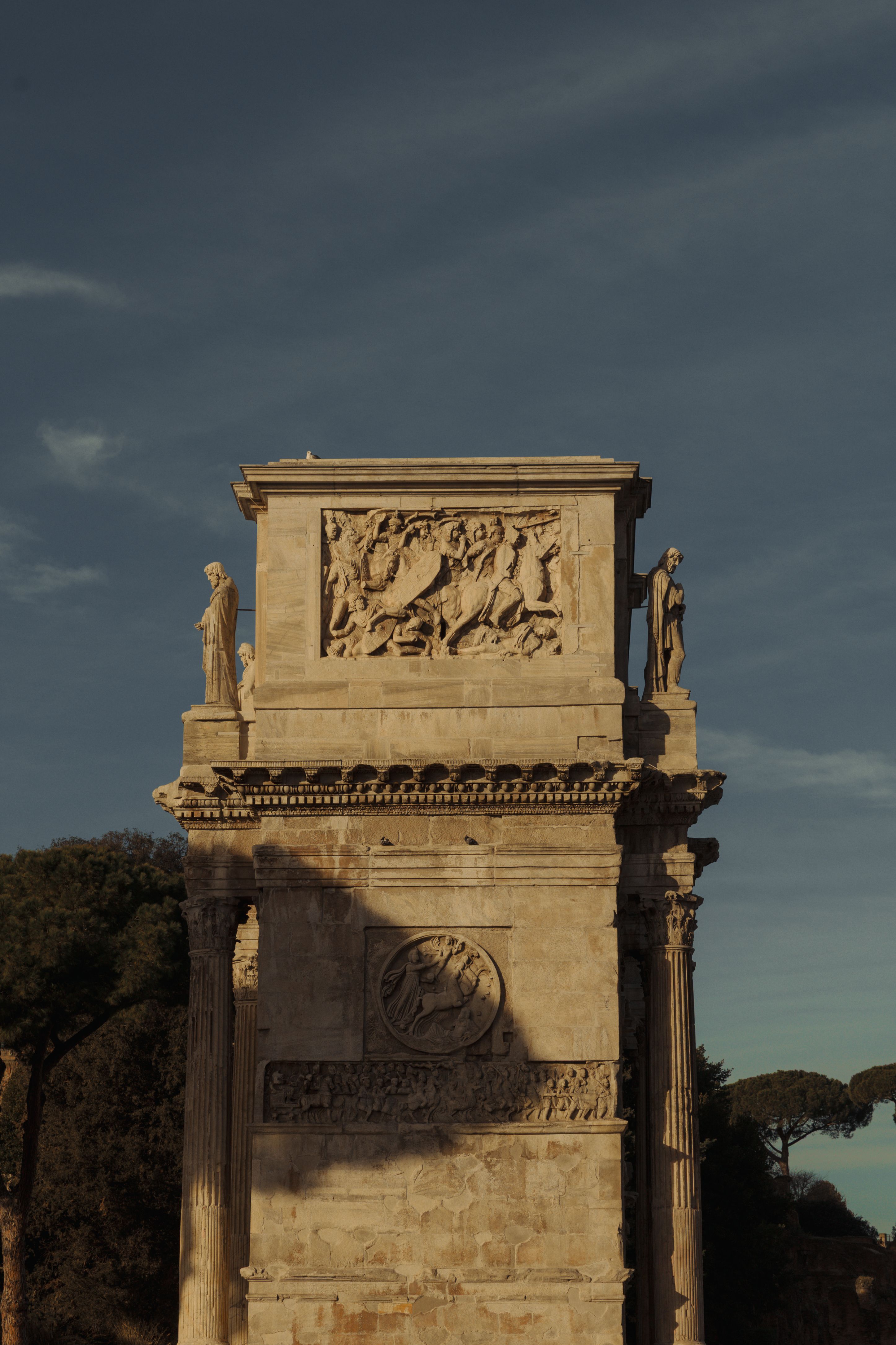Historic arch monument in Rome, captured with dramatic lighting against a clear sky.