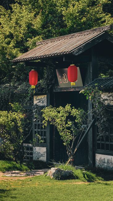 Serene entrance to a traditional Chinese garden adorned with red lanterns and lush greenery.