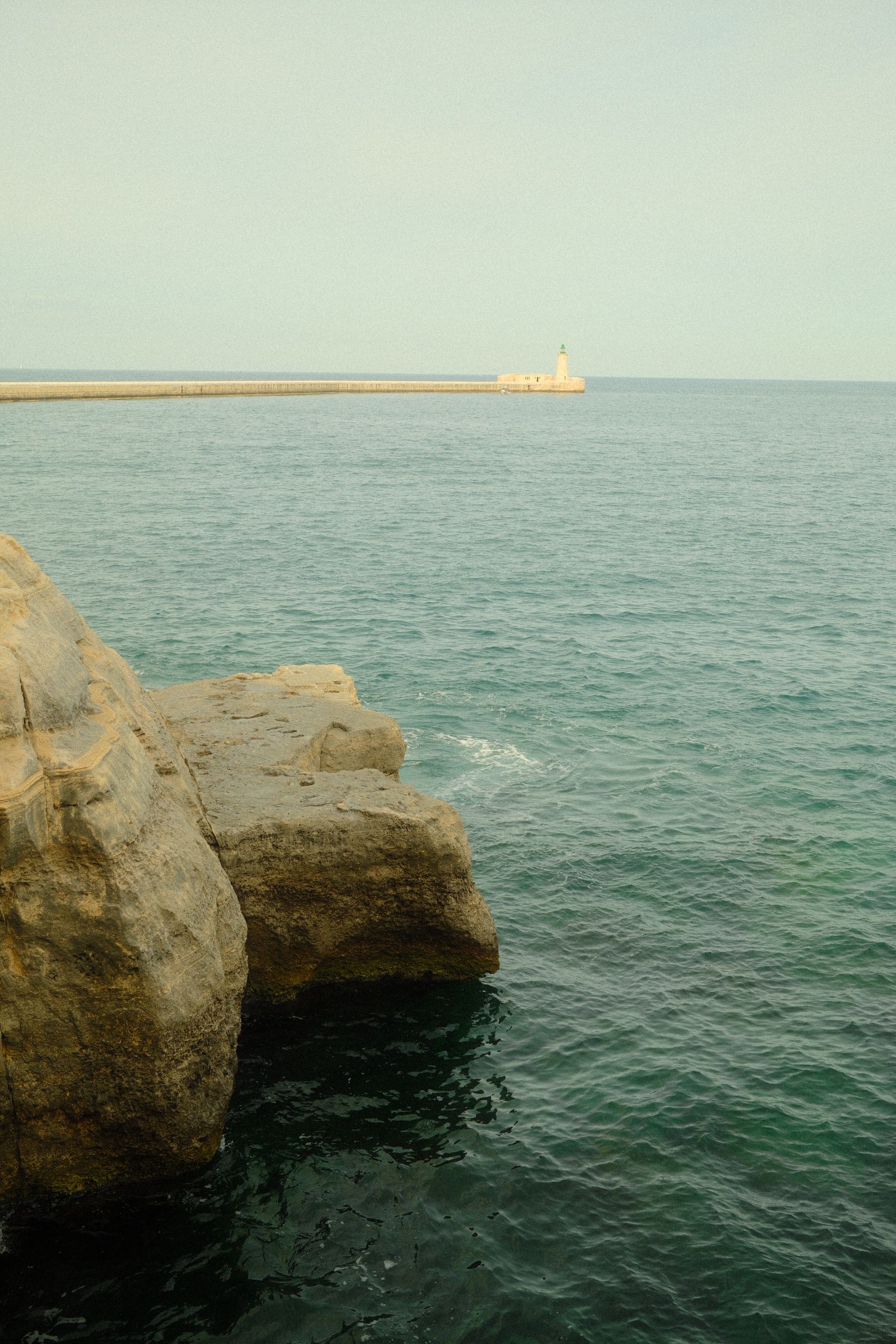 Peaceful seaside landscape in Malta featuring rocky cliffs and distant lighthouse.