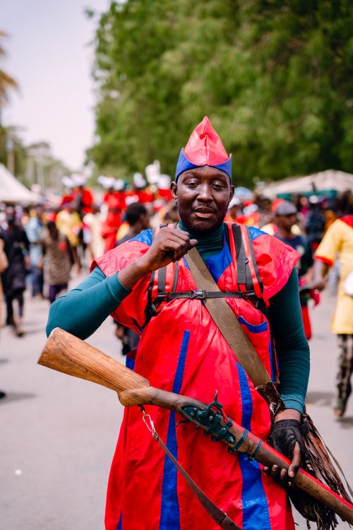 Free Man in vibrant traditional attire holding a rifle at a Nigerian festival parade. Stock Photo