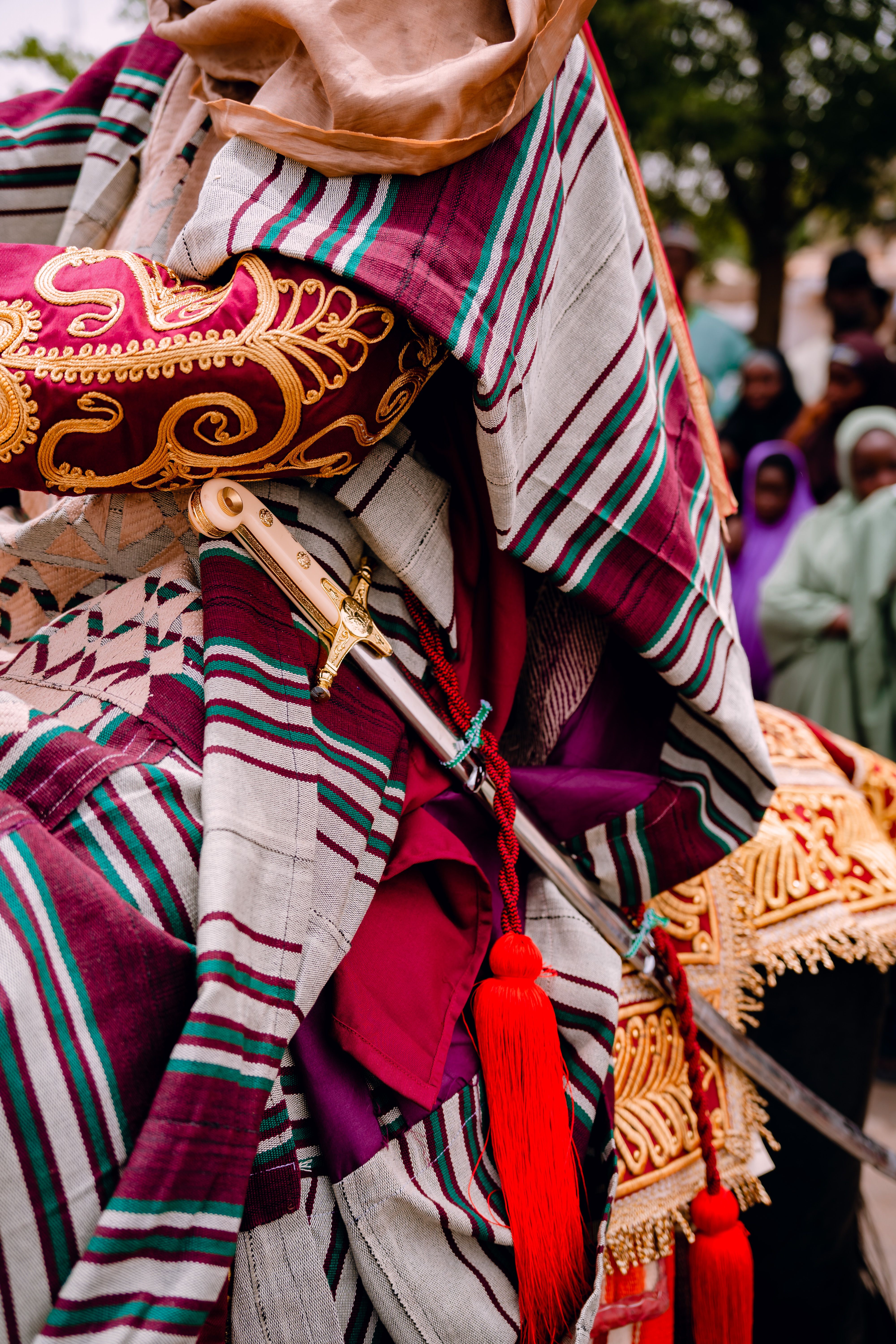 Close-up of a traditional Nigerian robe with detailed embroidery and vibrant red tassels during a cultural event.