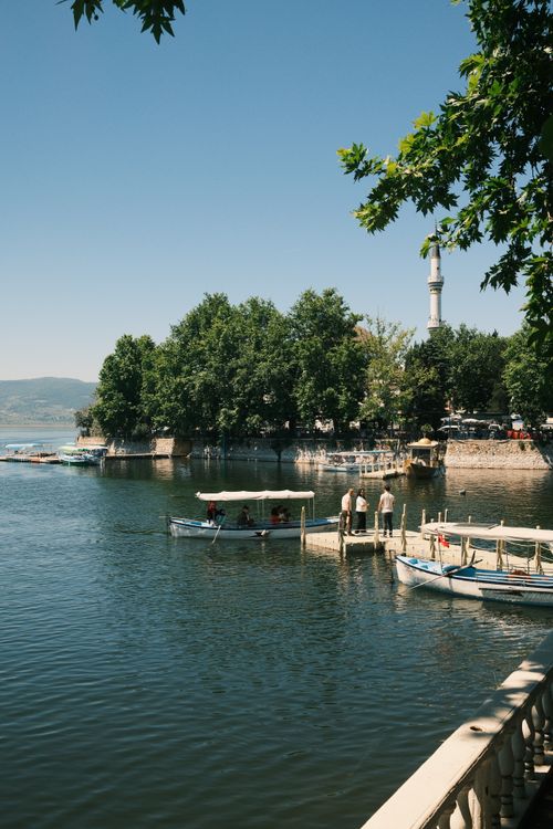 Free Tranquil lake scene in Bursa, Türkiye, featuring moored boats and a distant minaret surrounded by lush greenery. Stock Photo