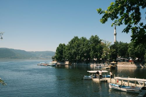 Free Scenic view of a lake with boats and a mosque in Bursa, Türkiye, under a clear blue sky. Stock Photo