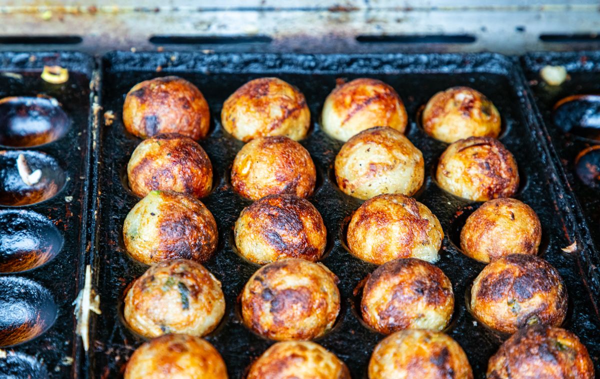 Takoyaki cooking on a traditional iron grill — Osaka's most iconic street food, addictive and blisteringly hot.