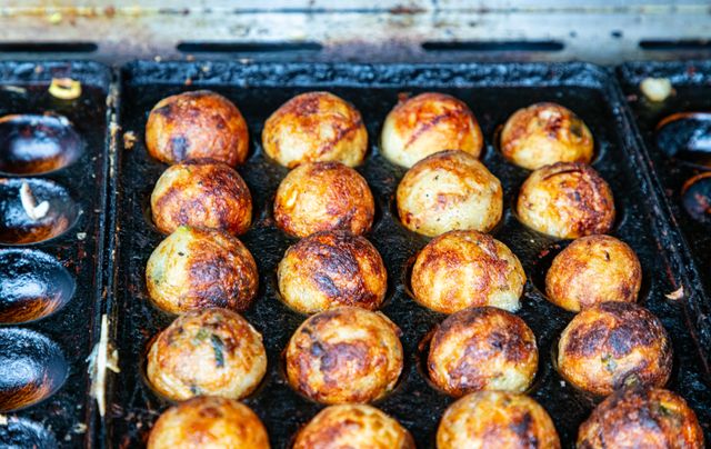 Rows of browned takoyaki balls cooking in a well-seasoned cast iron griddle