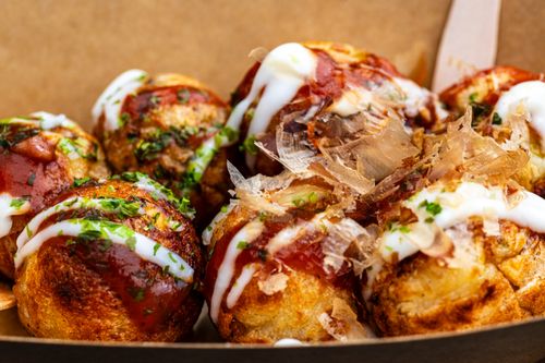 Free Close-up of freshly prepared takoyaki drizzled with sauce and bonito flakes, a Japanese street food delicacy. Stock Photo