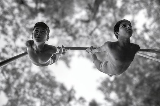 Black and white shot of two boys performing gymnastics on a horizontal bar outdoors.