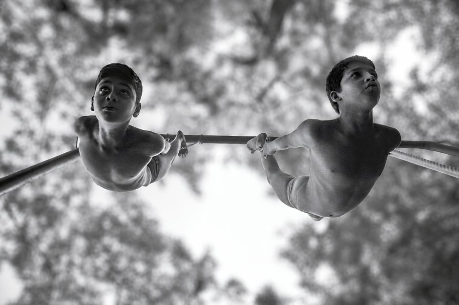 Black and white shot of two boys performing gymnastics on a horizontal bar outdoors.