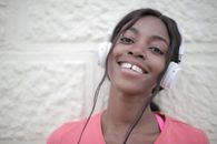 Positive young black female in bright t shirt wearing headphones and listening to music while looking at camera