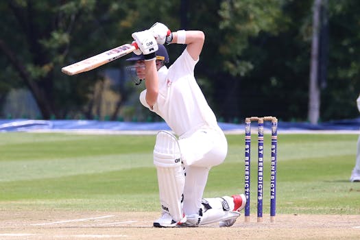 Cricketer in action performing a sweep shot on a sunny outdoor pitch.