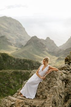 Woman in white dress posing on rocky mountain landscape, serene and elegant setting.