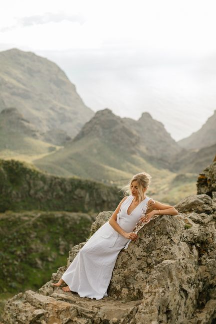 Woman in white dress posing on rocky mountain landscape, serene and elegant setting.