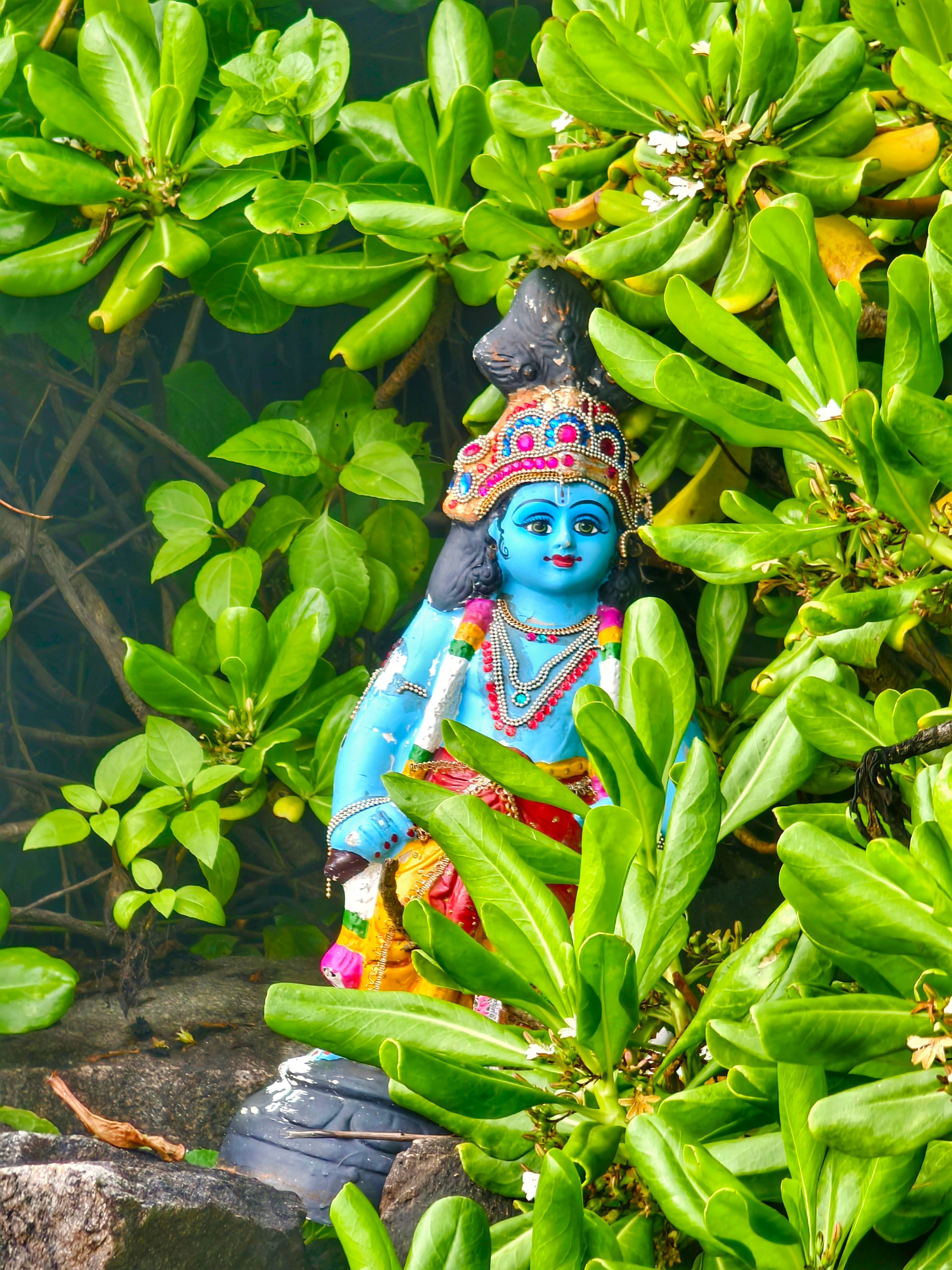 Vibrant Hindu deity statue amidst lush green foliage, providing a serene cultural scene.