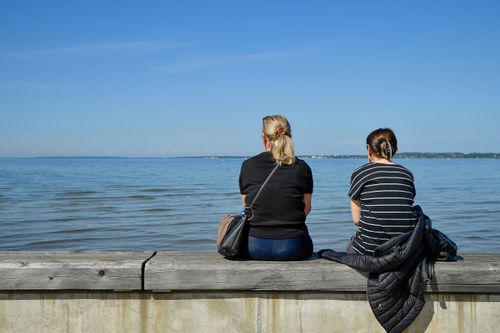 Free Two women sitting by Tallinn Bay, enjoying a peaceful seaside view under a clear blue sky. Stock Photo