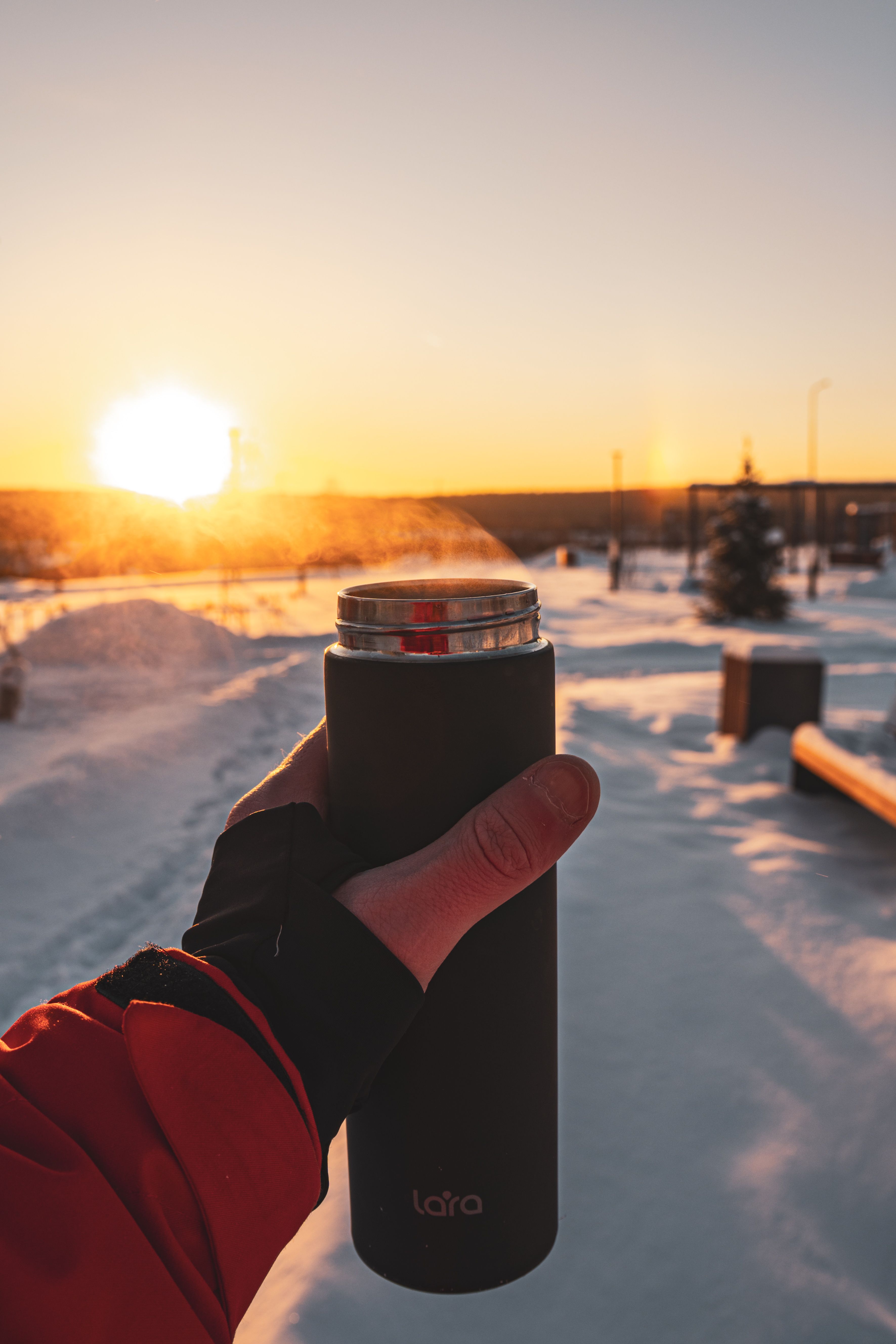 Steam rising from a thermos held in gloved hands against a winter night