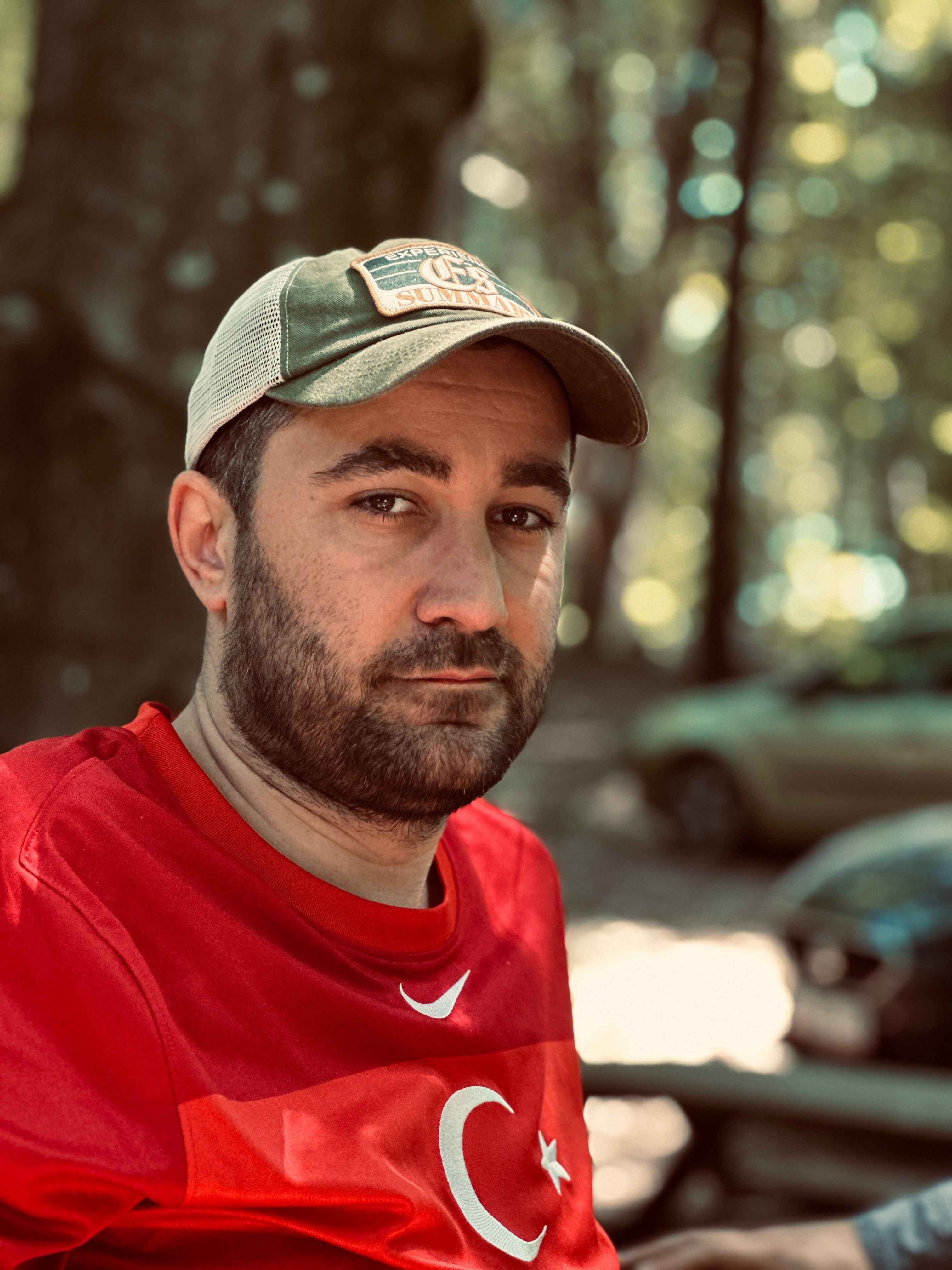 Man wearing a cap and Turkey flag shirt, outdoors in a sunlit Istanbul park.