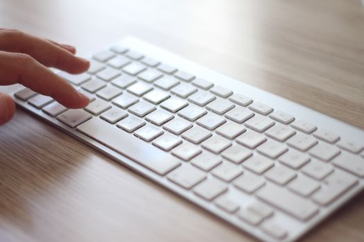 Close shot of a hand typing on a sleek white wireless keyboard, ideal for tech and blogging themes.