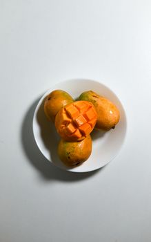 Chopped and whole mangoes on a white plate, showcasing the vibrant fruit.