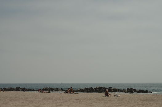 A tranquil beach view with people relaxing and a distant horizon on a cloudy day.