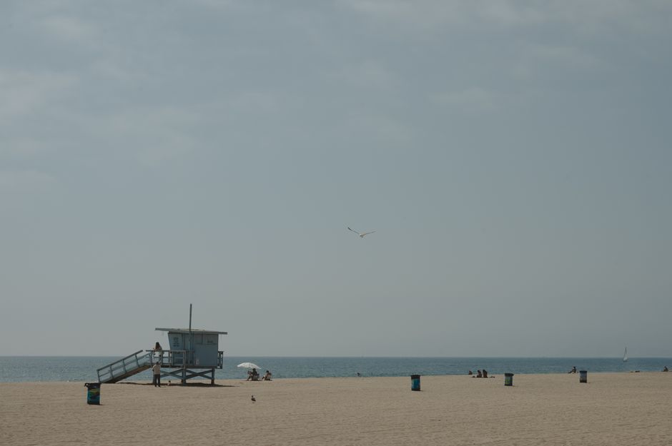 A peaceful beach scene featuring a lifeguard tower and scattered beachgoers under a clear sky.