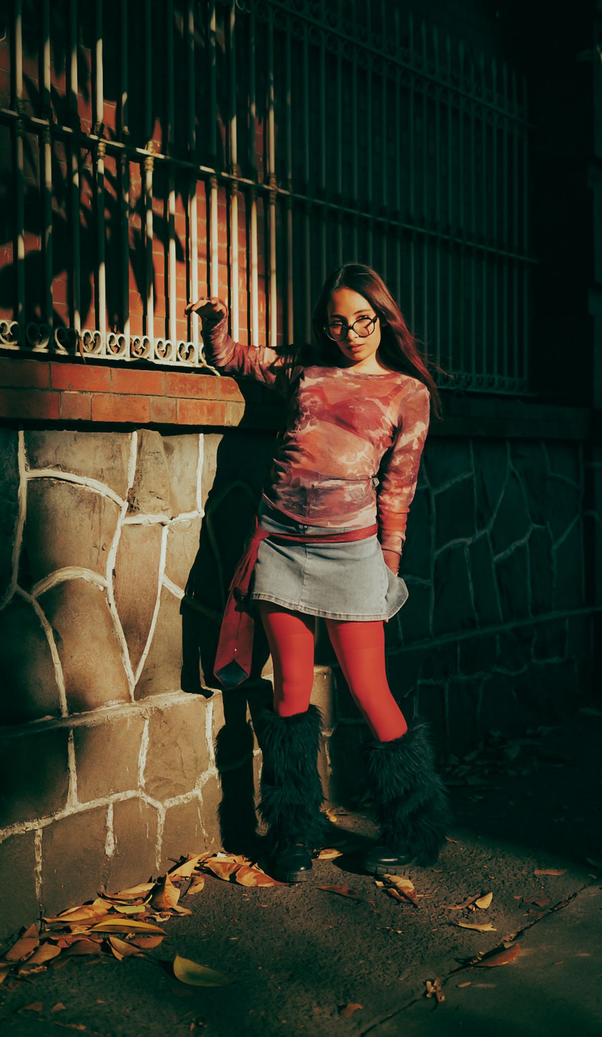 Stylish woman in colorful attire leans against brick wall on a sunny fall day in the city.