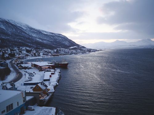 Free A stunning winter scene captures Tromsø's snowy harbor with distant mountains. Stock Photo