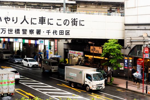 Bustling street view in Tokyo, Japan, with colorful umbrellas and vehicles during a rainy day.