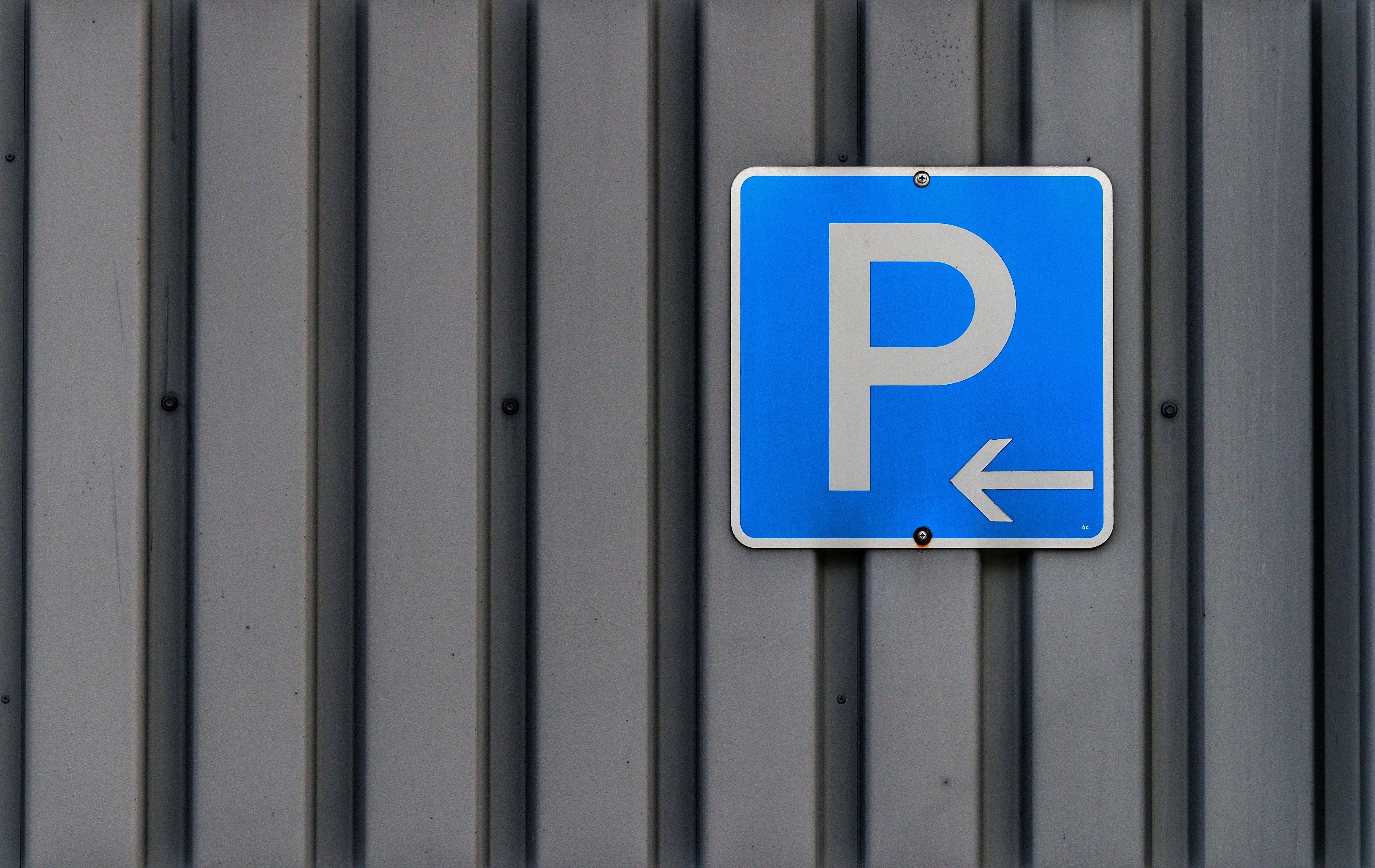 Closeup of a blue parking sign with arrow on a corrugated metal wall, outdoor setting.