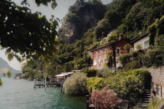A picturesque view of a villa by the beautiful Lake Lugano in Ticino, surrounded by lush greenery and mountains.