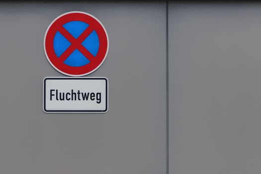 A German 'Fluchtweg' emergency exit sign with prohibition sign on a gray wall, offering clear copy space.