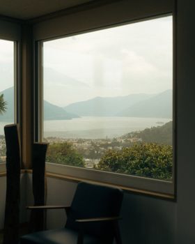 Peaceful scene of a lake and mountains seen through a room window in Ticino, Switzerland.
