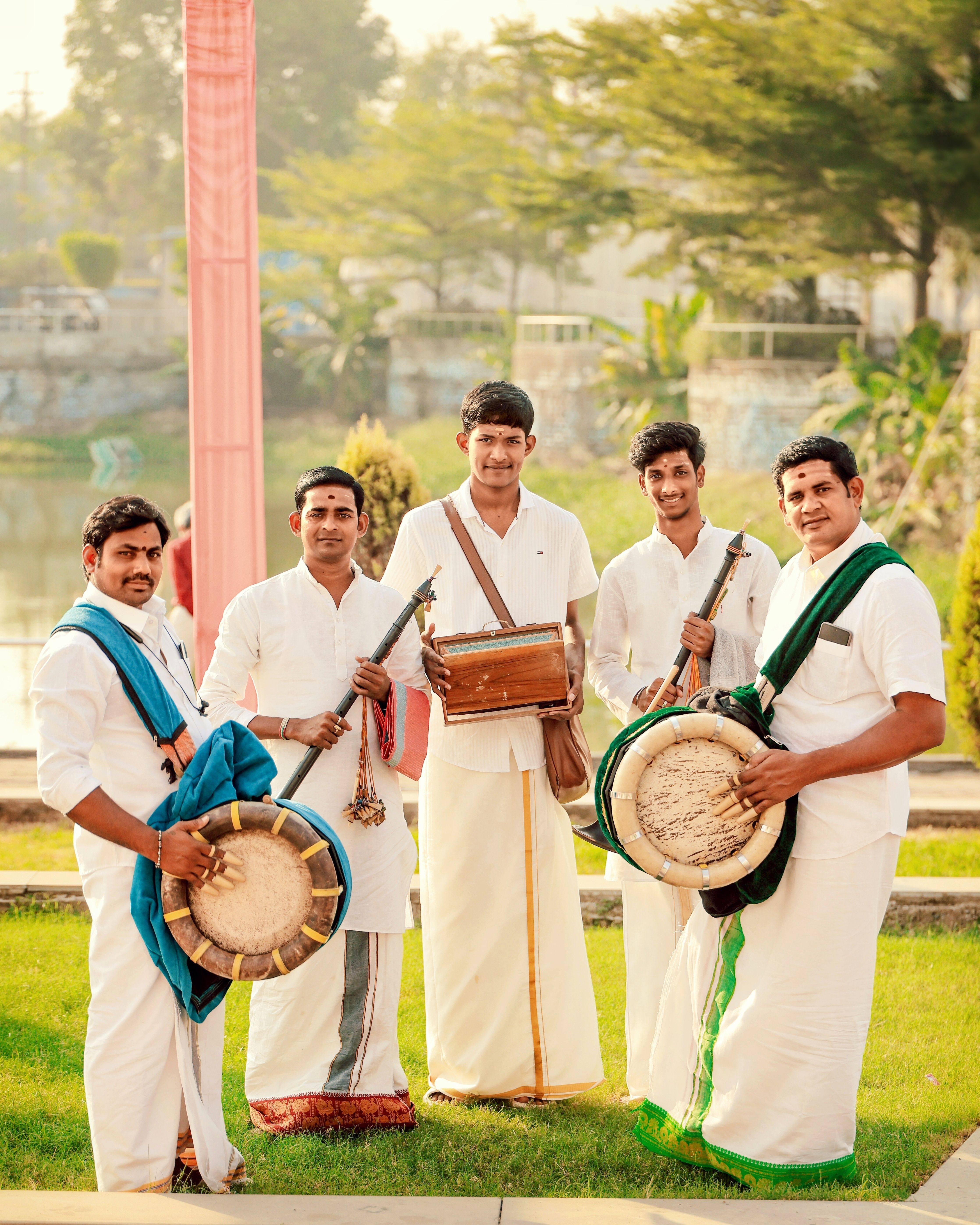 Group of men in traditional attire playing South Indian musical instruments outdoors.