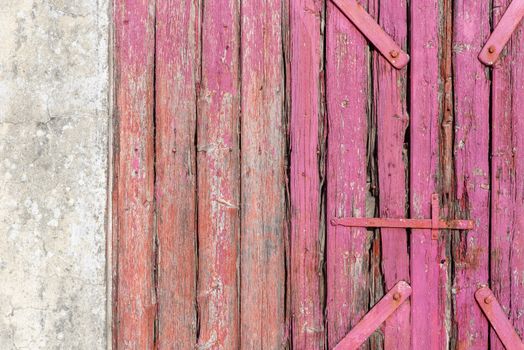 Closeup of a weathered pink wooden door with rustic textures showcasing aging wood and metal hinges.