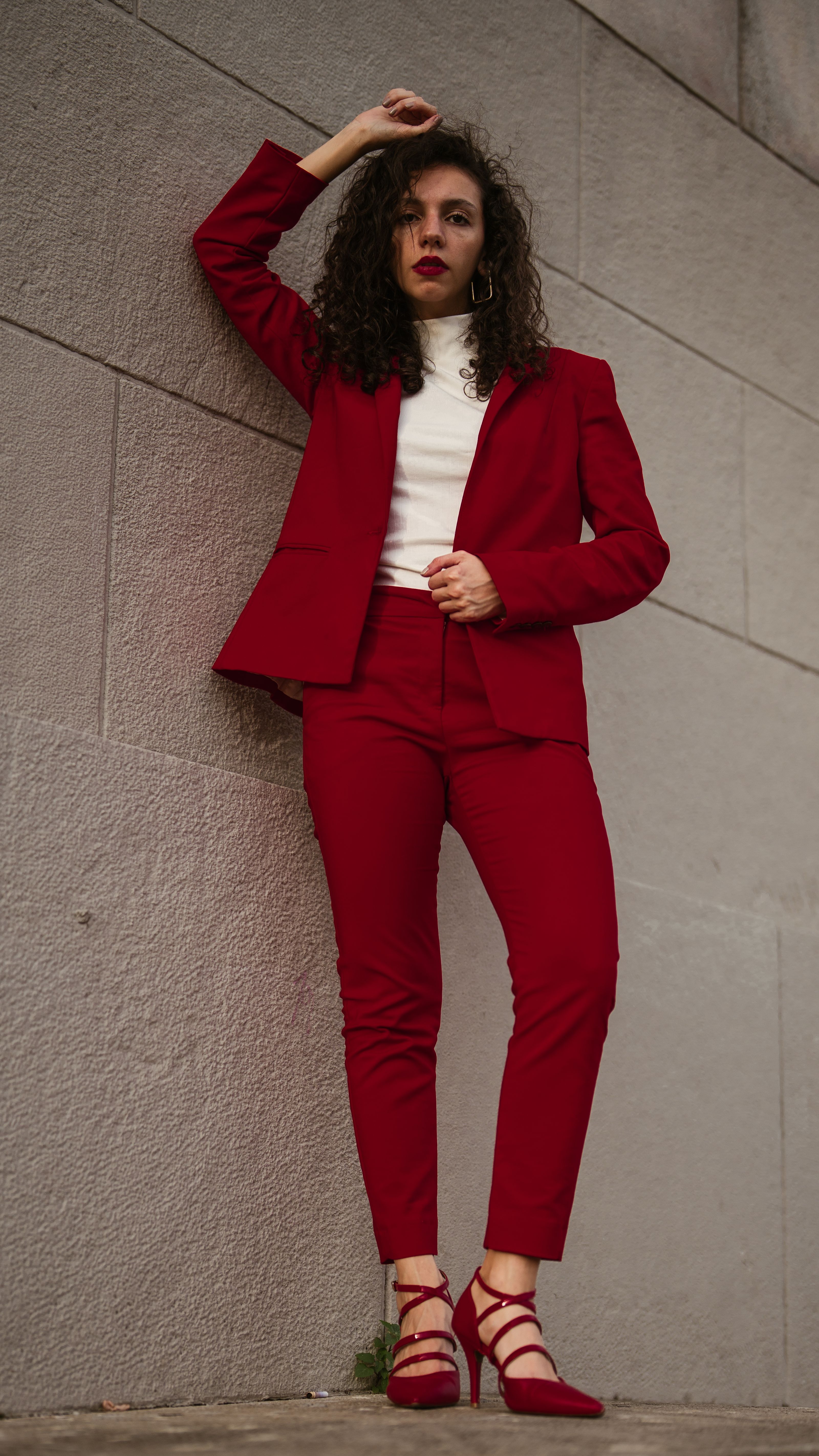 Mulher elegante em um terno vermelho stands com confiança contra uma parede de concreto em Buenos Aires.