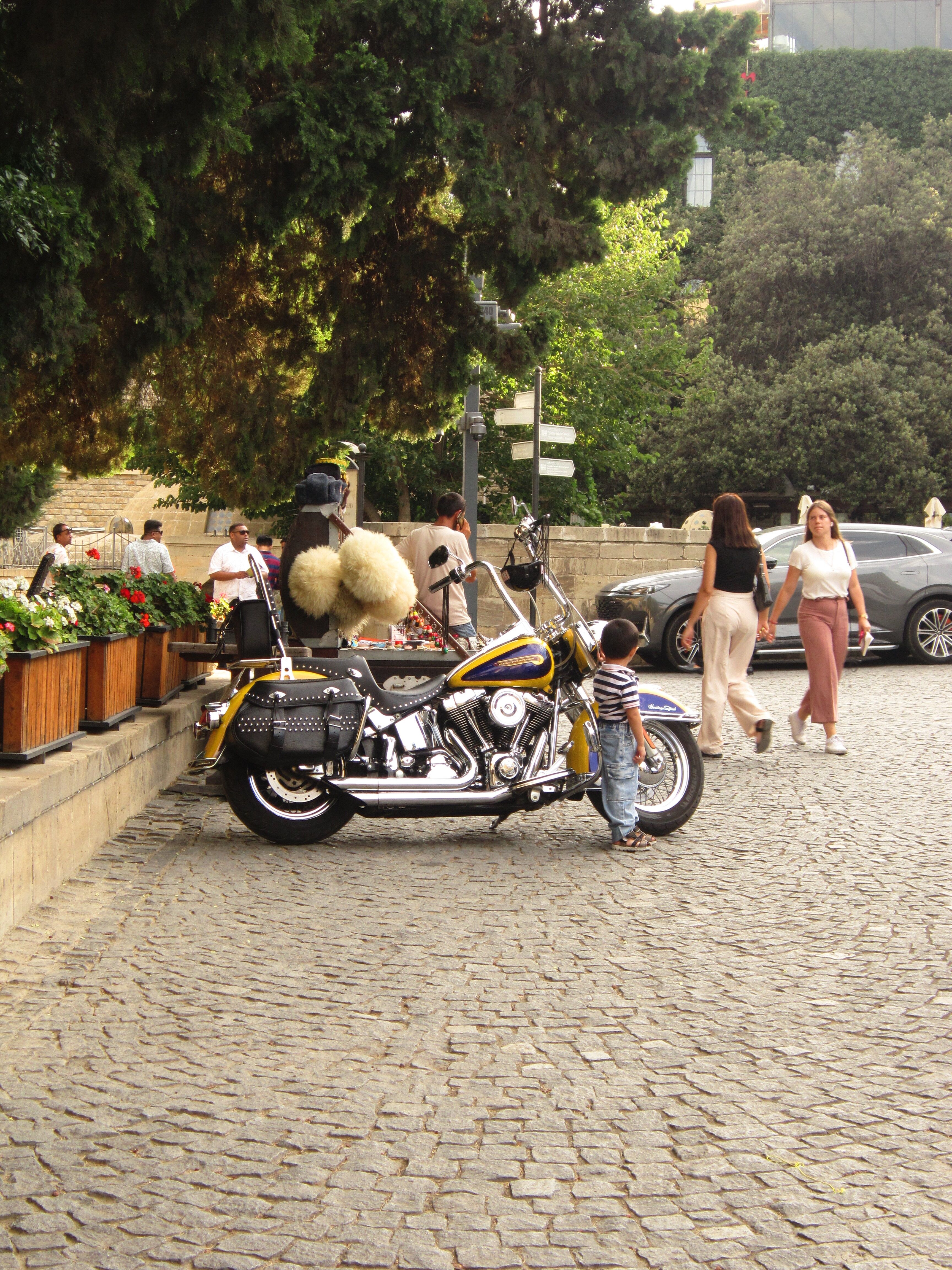 Motorcycle parked on cobblestone street with passersby, outdoors on a sunny day.