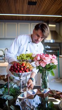 Chef in a modern kitchen arranging fresh fruit and roses for an elegant display.