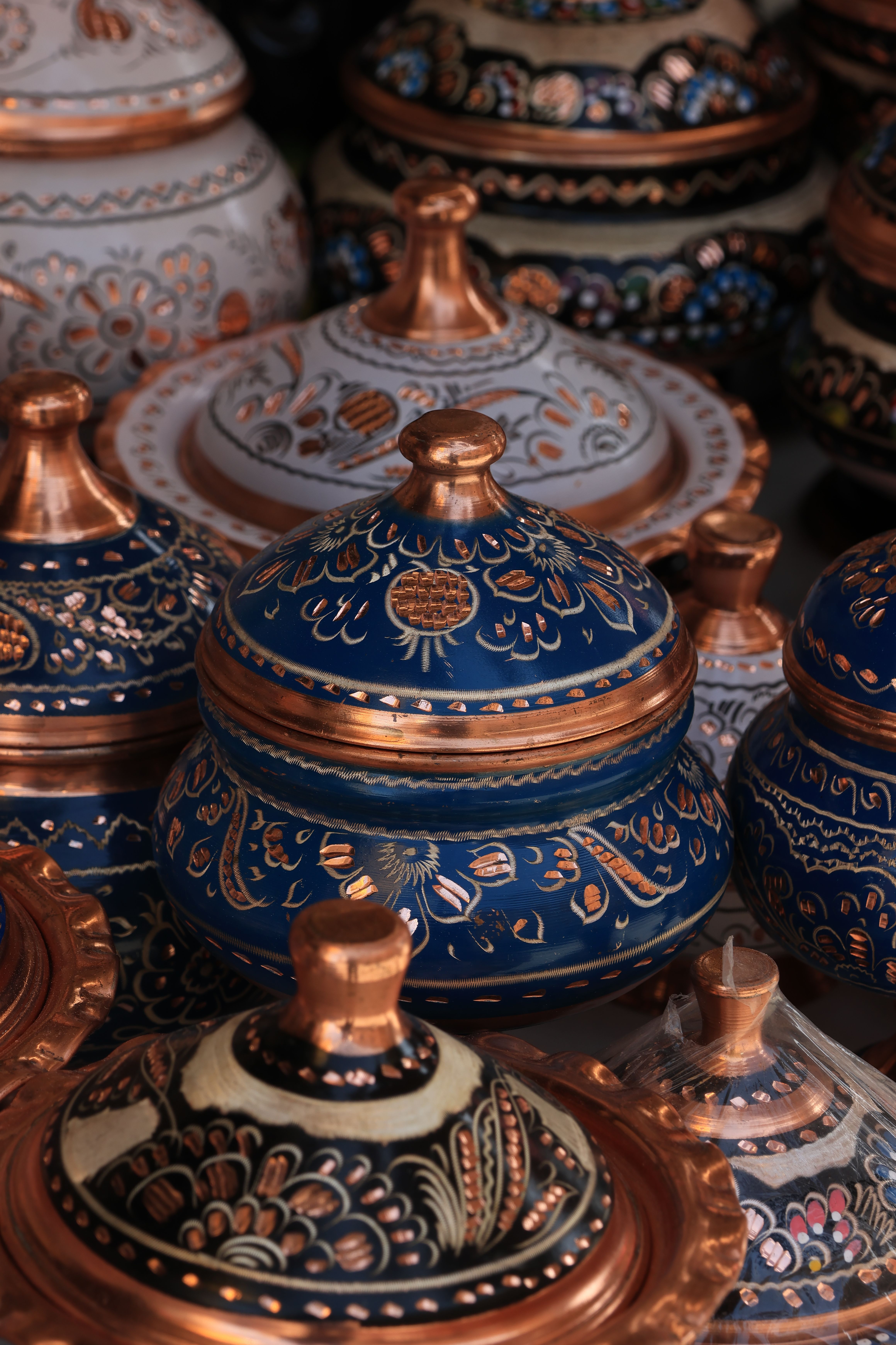 A vibrant array of traditional hand-painted ceramic pots with intricate designs and metallic accents.