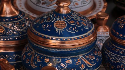 A vibrant array of traditional hand-painted ceramic pots with intricate designs and metallic accents.
