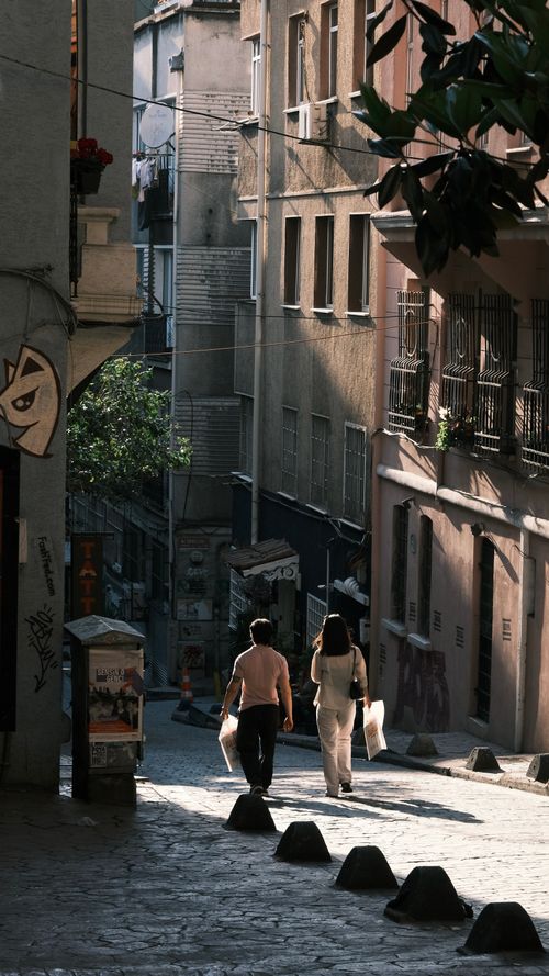 Free A couple strolls down a sunlit historic street in İstanbul, Türkiye, in the early evening. Stock Photo